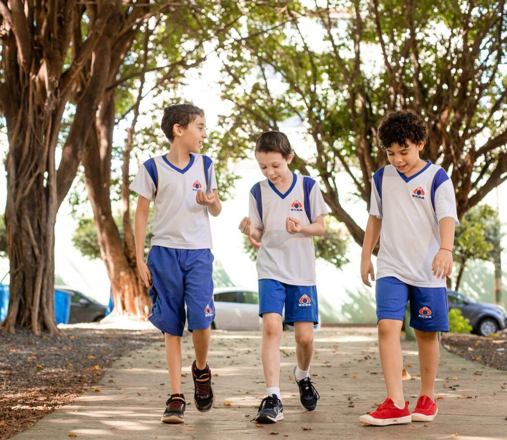 Crianças uniformizadas andando à caminho da escola felizes